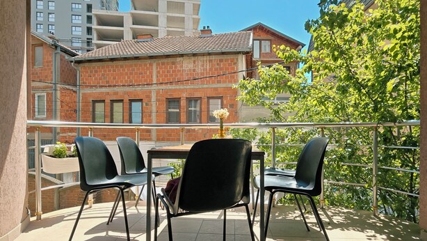 Un balcon avec une table et des chaises, un luminaire suspendu et une vue sur des immeubles et des arbres.