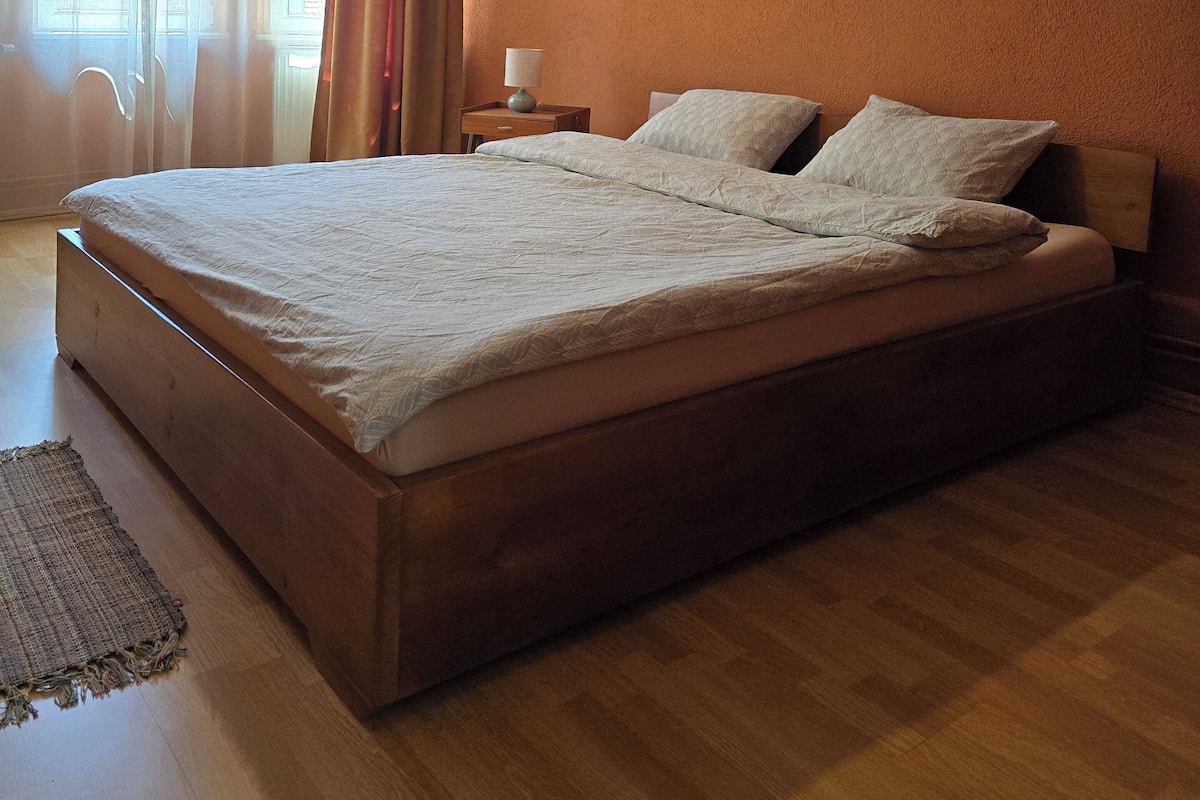 Un dormitorio con una cama grande, una mesita de noche, una lámpara y una ventana con cortinas.