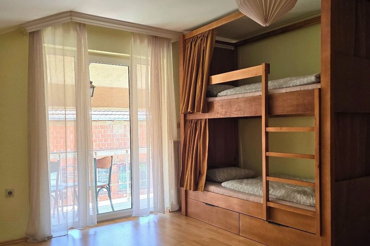 Una habitación con una cama litera de madera, una puerta corrediza de vidrio a un balcón y una lámpara colgante.