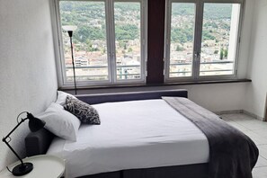 A bedroom with a bed, a bedside lamp, a window with a view of a cityscape. - A few steps from the center of Locarno (Loft Torre 2) (Locarno)