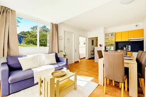 Ein modernes Wohnzimmer mit einer Couch, einem Couchtisch und einem Essbereich mit Stühlen, im Hintergrund eine Küche.