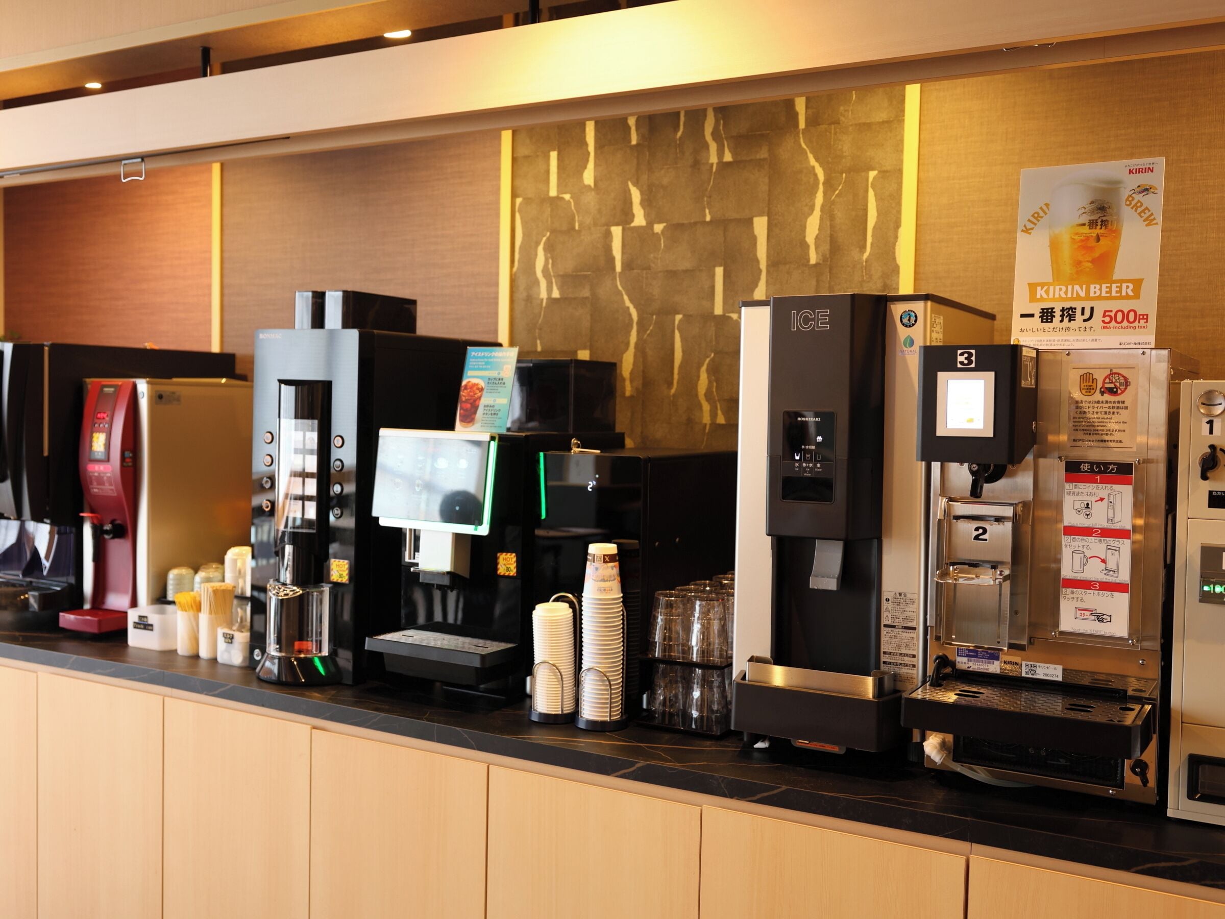 A coffee station with various machines, including an ice dispenser and a beverage dispenser, with a sign advertising Kirin beer.