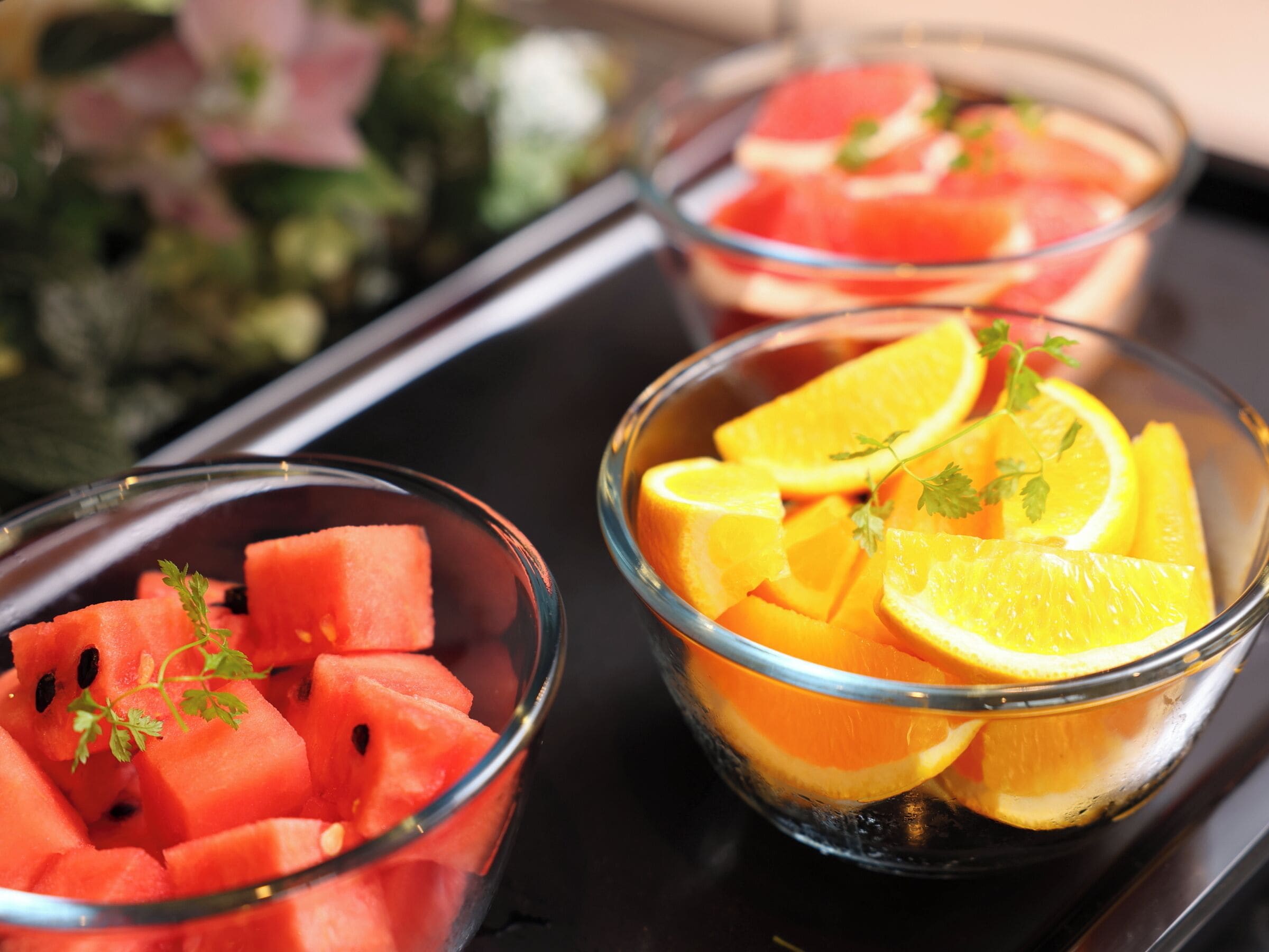 Trois bols en verre contenant des morceaux de pastèque et des tranches d’orange.