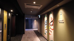 A hotel hallway with carpeted floors, a wall-mounted air conditioning unit, and colorful wall art. - Dormy Inn Komatsu Heihou-no-Yu (Komatsu)
