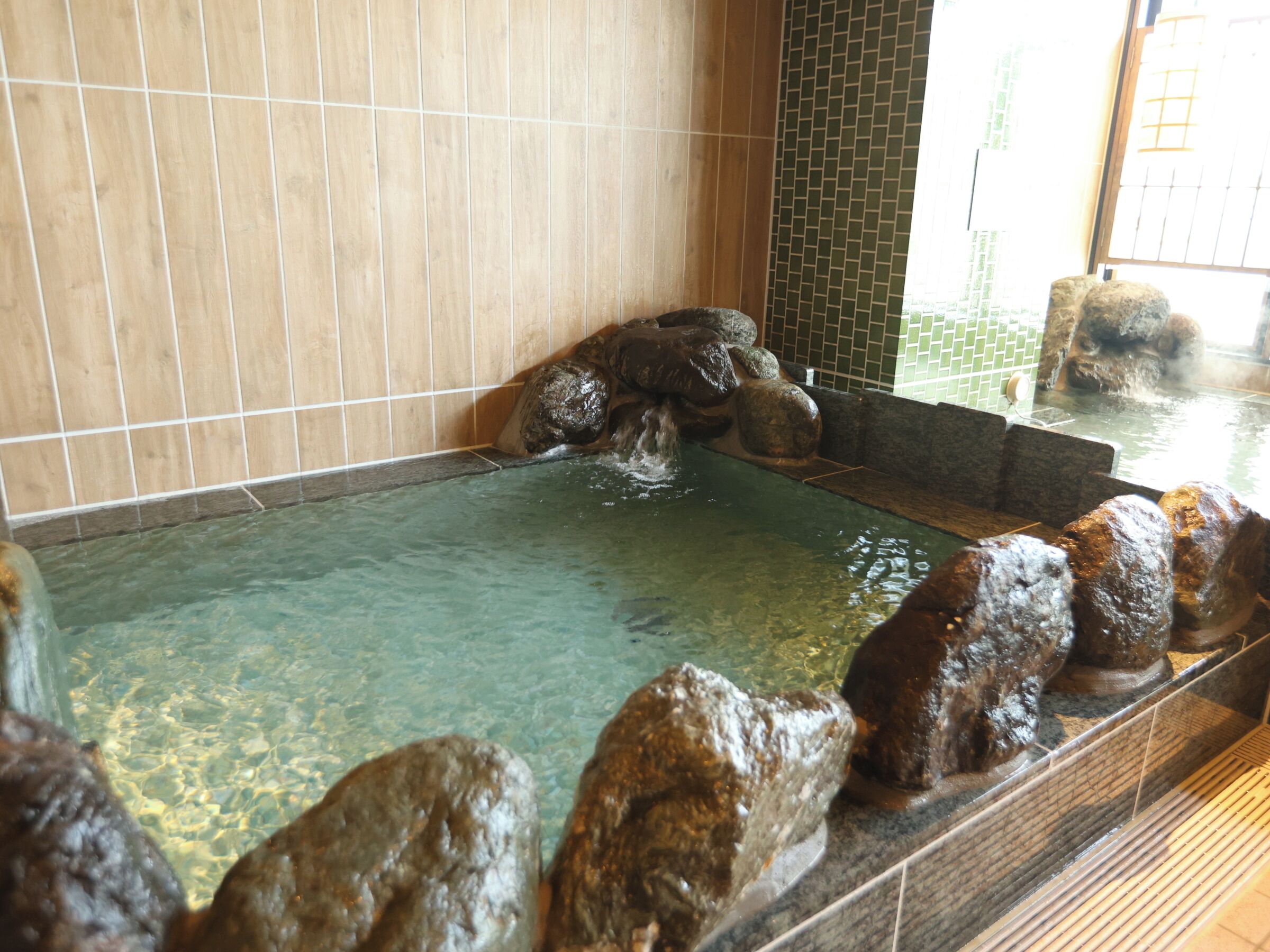 Un área de aguas termales con agua cristalina, rocas y paredes con azulejos.