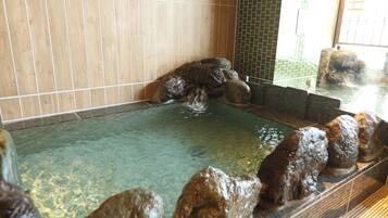 A hot spring area with clear water, rocks, and tiled walls.