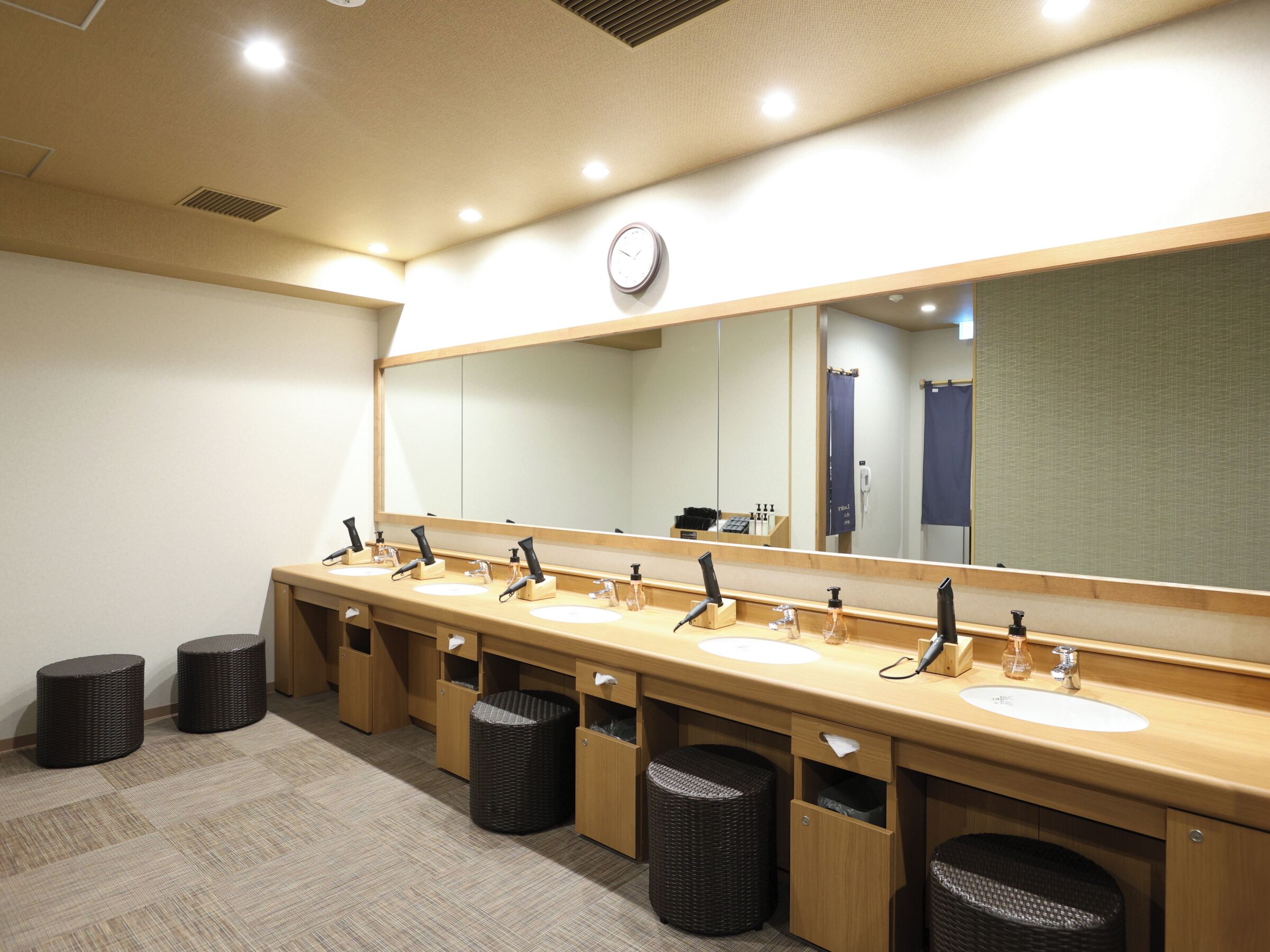 A long, wooden vanity with multiple sinks and mirrors, wooden cabinets, and waste baskets.