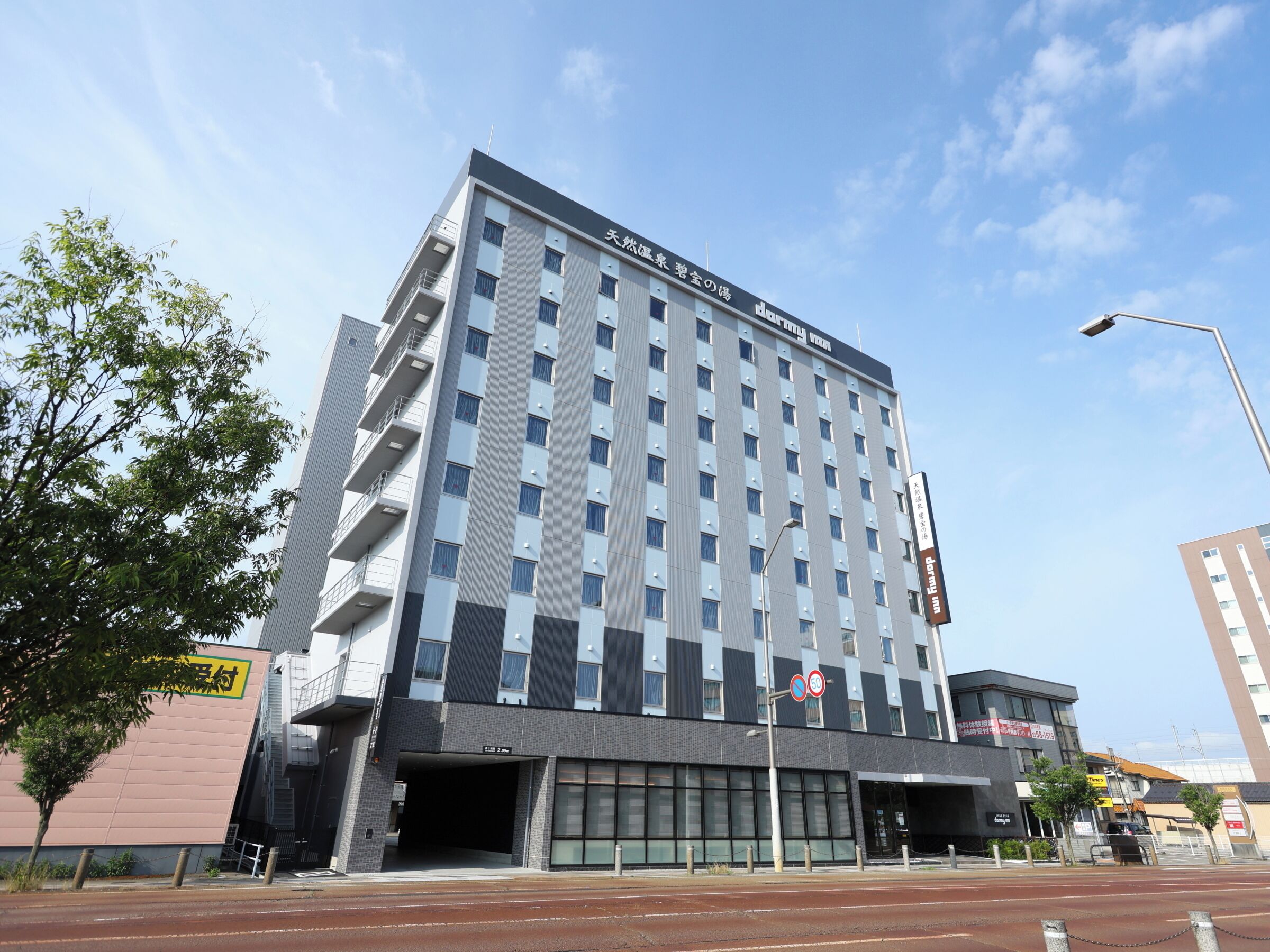Un hotel de varios pisos con un diseño arquitectónico moderno, destacándose una entrada imponente y un cielo despejado.