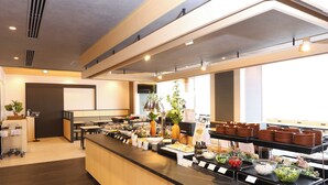 A modern buffet setup with a variety of food items, a seating area, and a large window providing natural light. - Dormy Inn Komatsu Heihou-no-Yu (Komatsu)