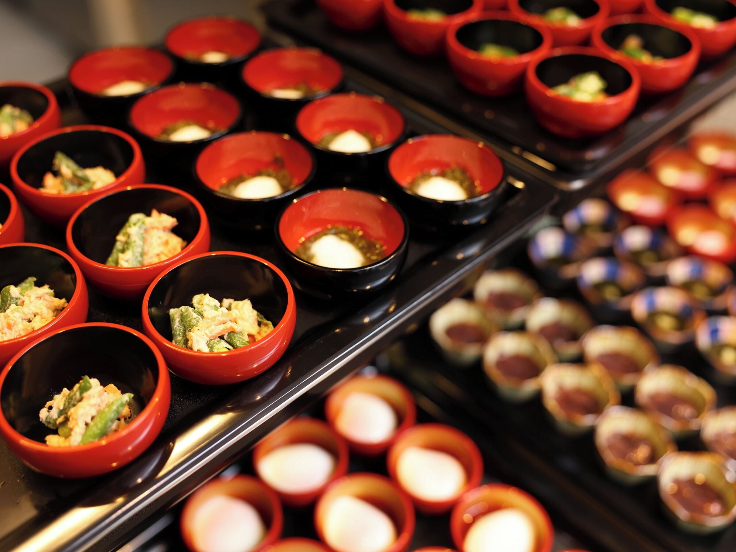 A variety of food items in small red and black bowls arranged on a tray.