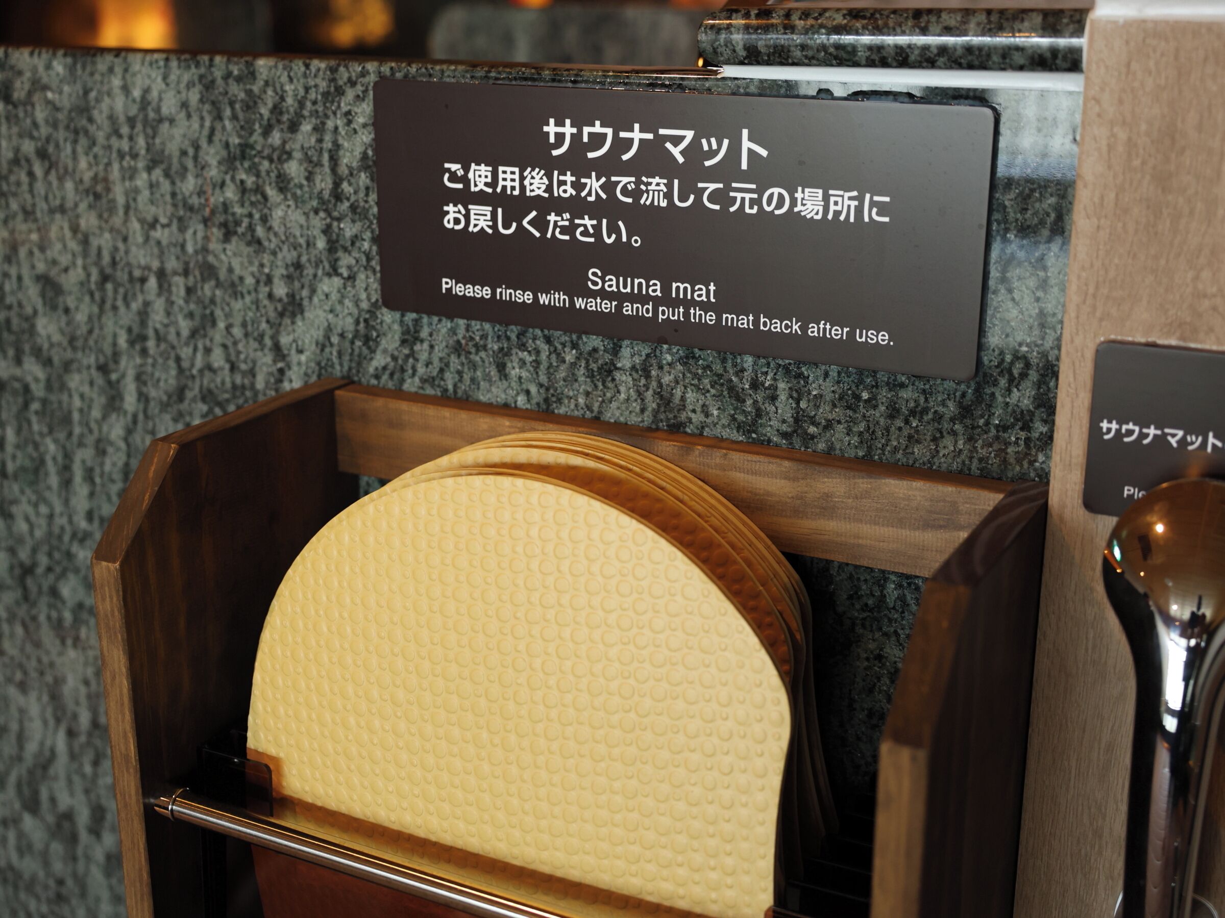 A wooden sauna mat holder with a sign instructing to rinse with water and put the mat back after use.