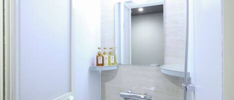 A narrow, white-walled bathroom with a shower, a toilet, and a shelf with toiletries.
