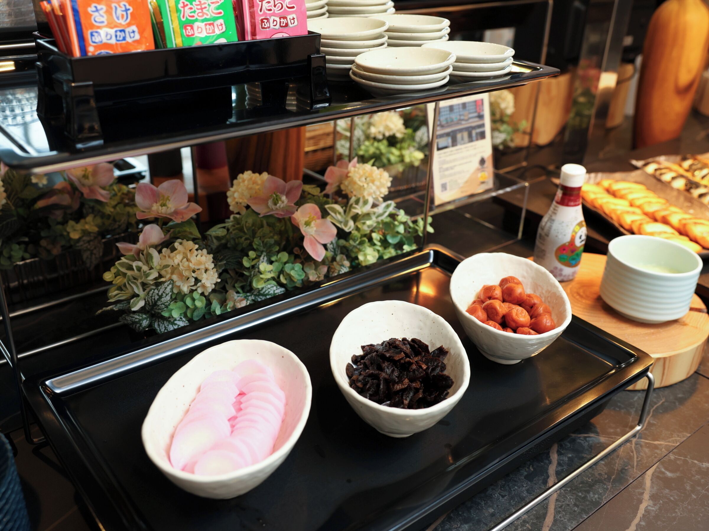 A buffet with various food items, including bowls of sliced fruits and nuts, and a display of plates and napkins.