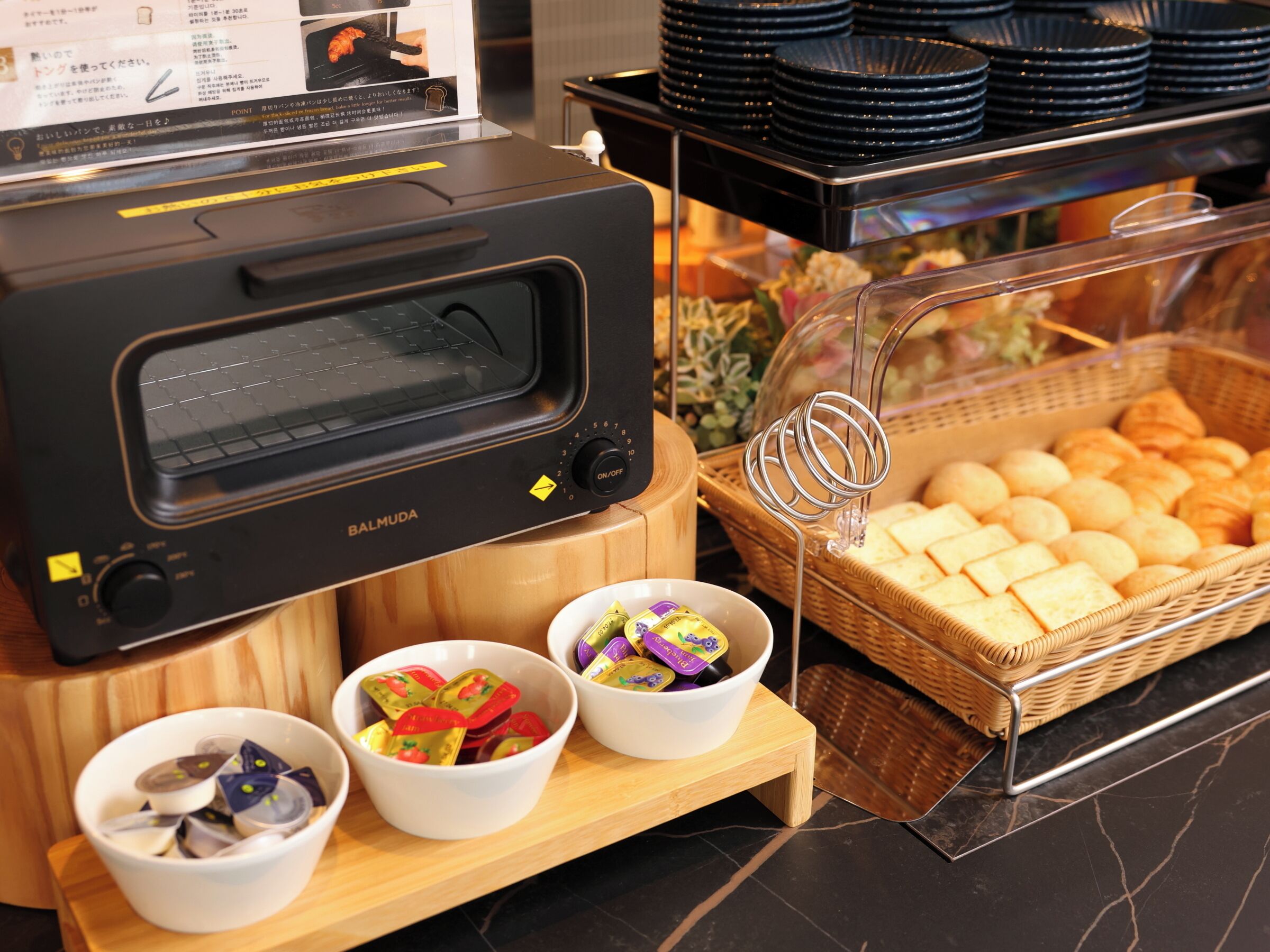 En buffetopstilling med en toasterovn, skåle med snacks og en kurv med brød.
