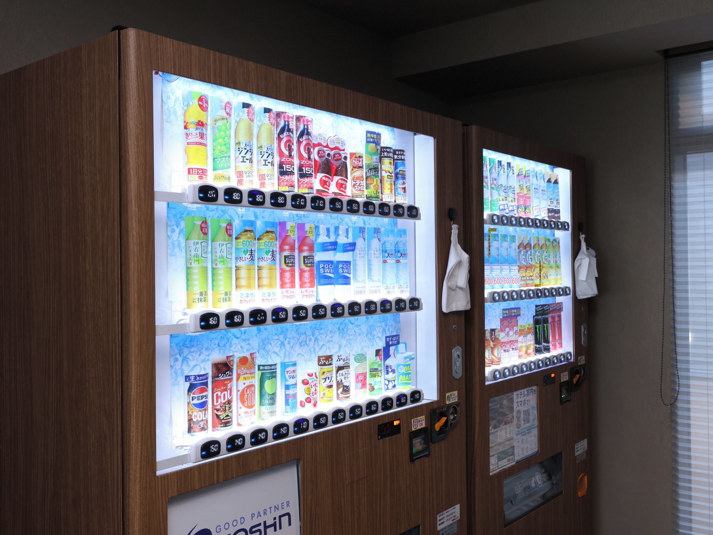 Vending machines with various beverages and snacks, a 'Good Partner' sign, and a window with blinds.