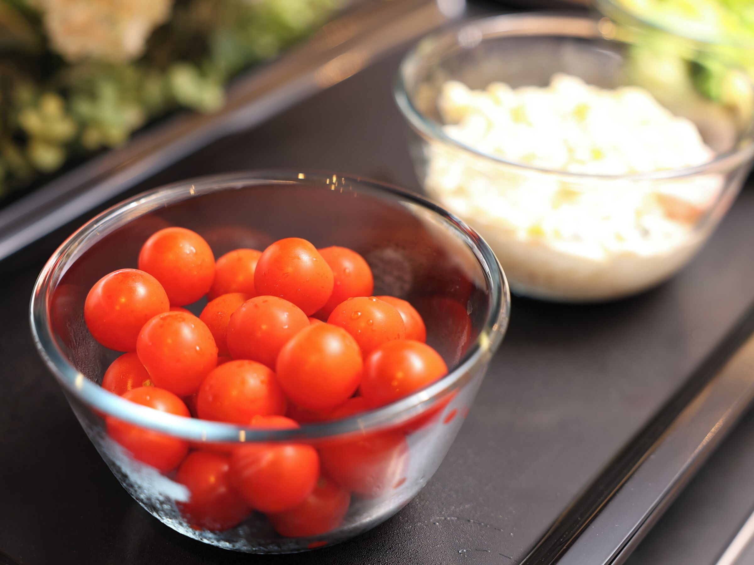 Un tazón de vidrio lleno de tomates cherry sobre una superficie negra.