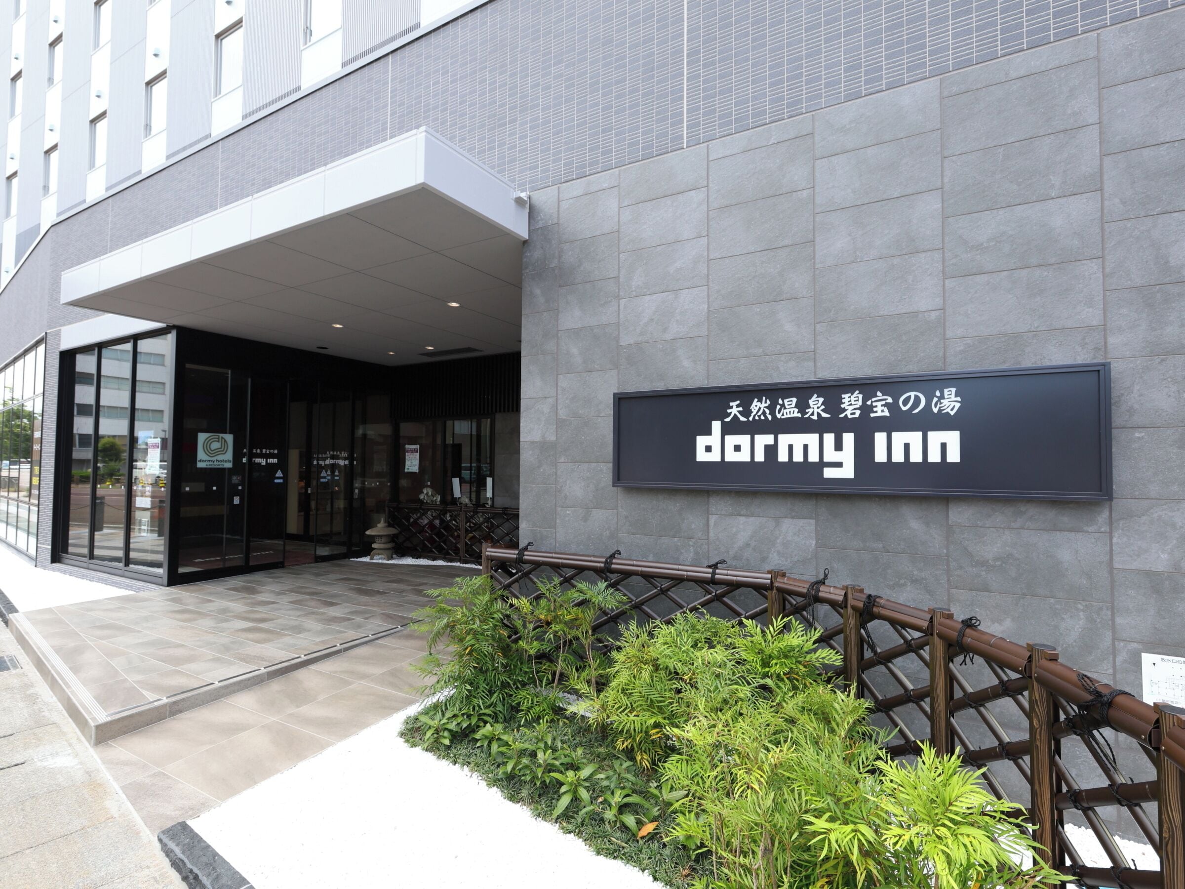 Ein modernes Gebäude mit einem Schild für 'dormy inn' und einem verschlossenen Eingang.
