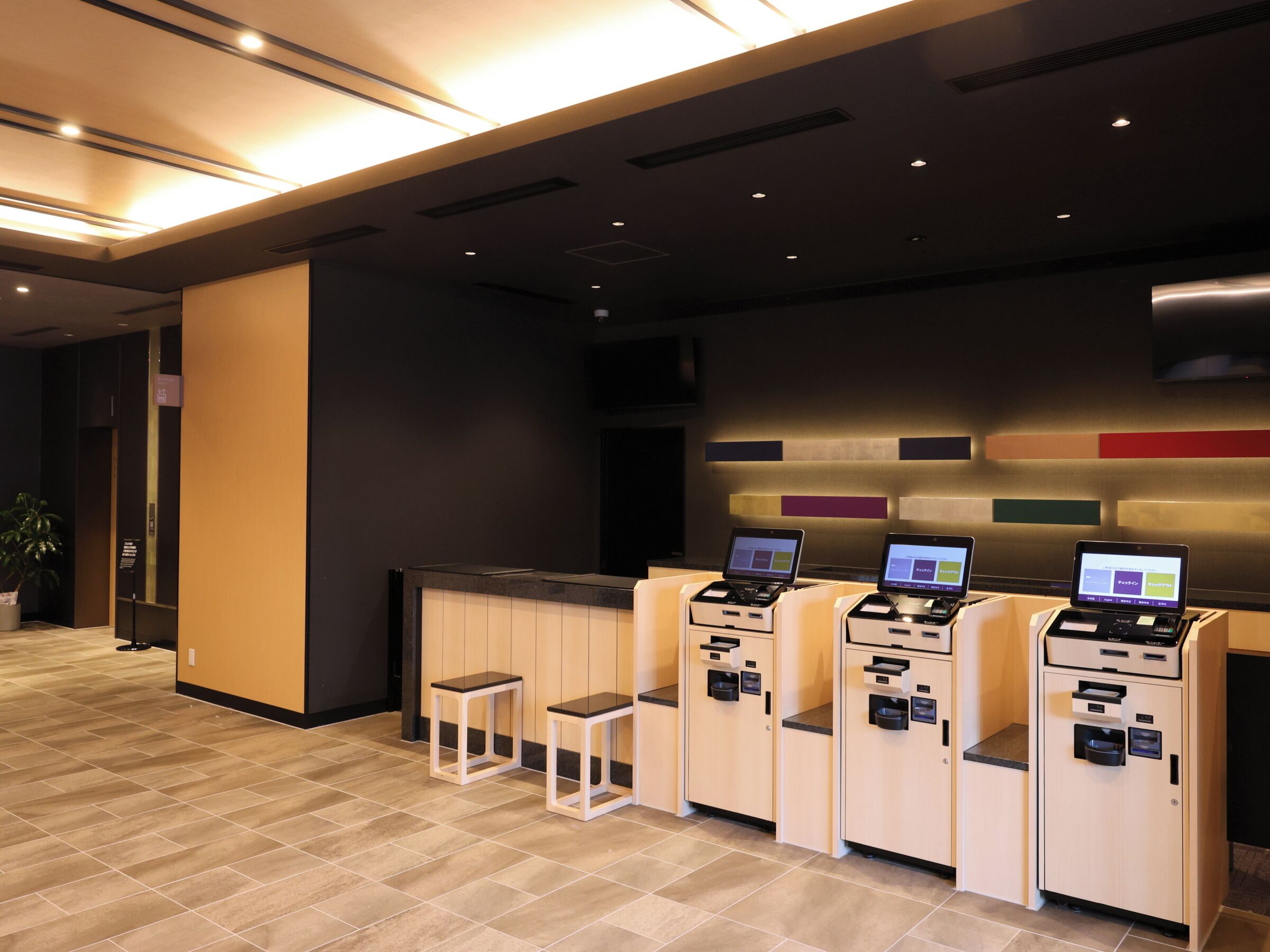 Una moderna area di reception con un bancone, tre chioschi self-service e una piccola zona salotto.