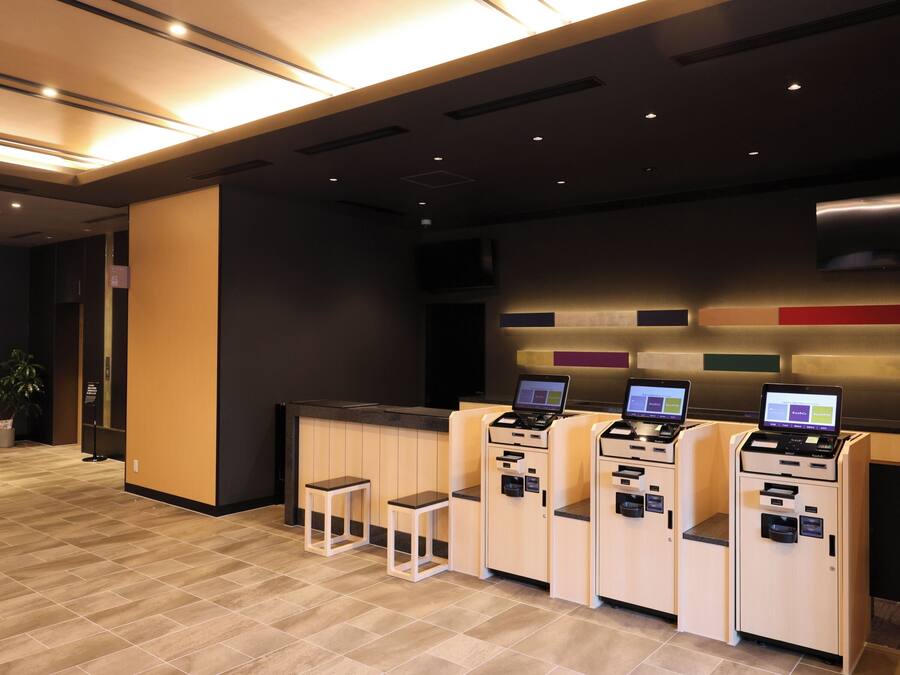 Una moderna area di reception con un bancone, tre chioschi self-service e una piccola zona salotto.