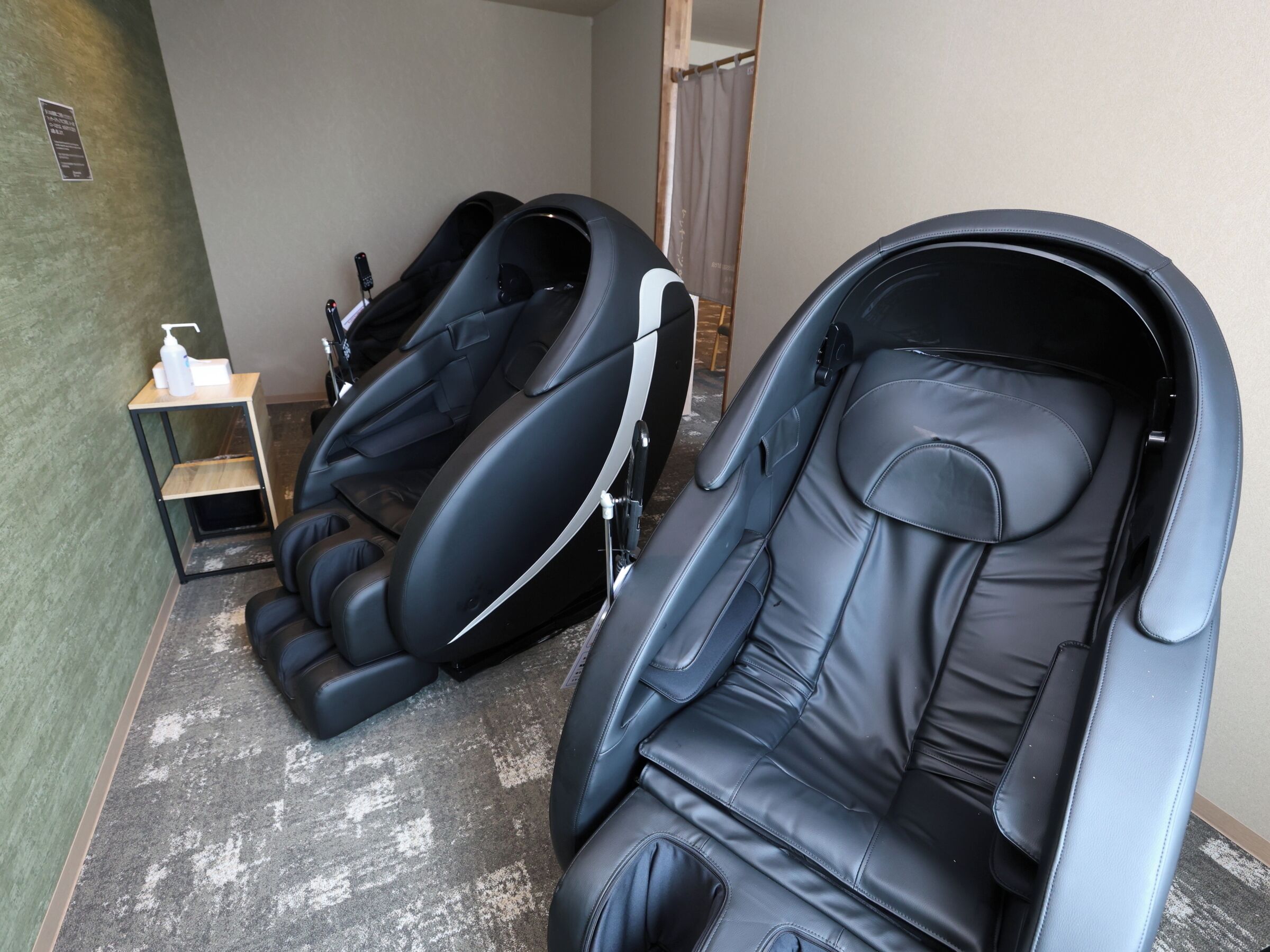 Une pièce avec deux fauteuils de massage, une petite étagère sur laquelle se trouve une bouteille, et une porte en bois.