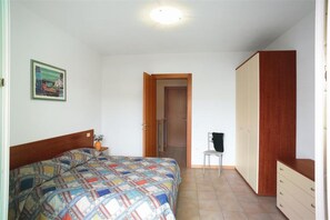 Un dormitorio con cama, una silla, un armario y una puerta que da a otra habitación.