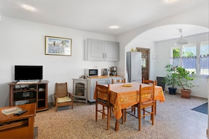 A compact living space with a dining area, kitchenette, television, and a potted plant.