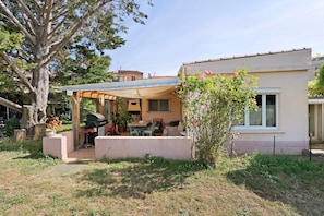 Una casa con porche cubierto, barbacoa y jardín.