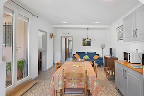 A dining area with a table, chairs, a sofa, and a kitchenette.
