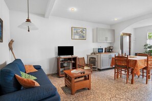 Un espacio habitable compacto con sofá, mesa de centro, televisor, kitchenette, mesa de comedor y sillas.