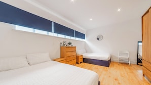 A bedroom with a large bed, a wooden dresser, a small bedside table, a nightstand, a white chair, and a window with a view. - Central - Stay 4 - Paid Parking - Near Transport (Maidstone)
