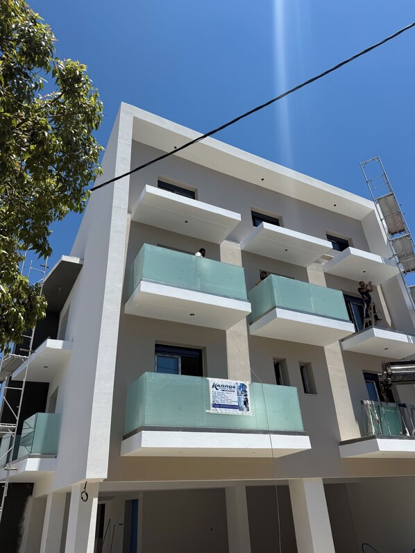 A multi-story building with balconies, a visible sign, and construction scaffolding. - Olympus Hospitality (Rhodes)