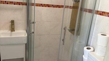 Una ducha con puerta de cristal, un lavabo blanco y un inodoro con papel higiénico.