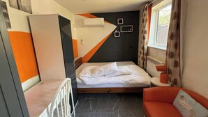 Ett kompakt hotellrum med en säng, en liten sittgrupp, ett element och ett fönster med gardiner.