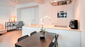 Una cocina moderna con armarios blancos, una isla central con una orquídea en maceta, una cafetera y un horno empotrado.