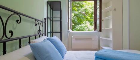Une chambre à coucher avec un lit, des oreillers, une fenêtre, un radiateur et une armoire.