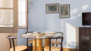 A dining area with a round glass table, four chairs, and a cabinet with a television. - Casa Nicole - fine stay in Navigli district (Milano)
