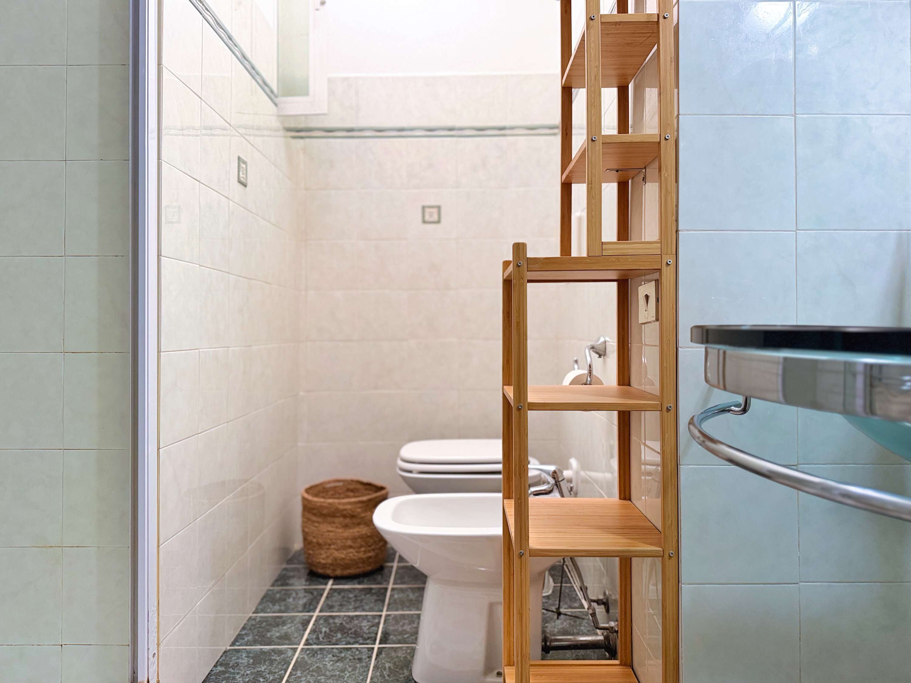Een badkamer met toilet, een douchetoilet, een houten plankunit en een metalen handgreep.