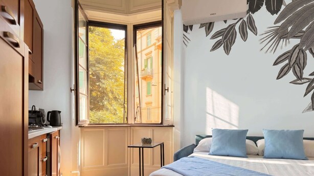 A bedroom with a bed, pillows, a small table, a window, and a wall with a leaf pattern. - Casa Nicole - fine stay in Navigli district (Milano)