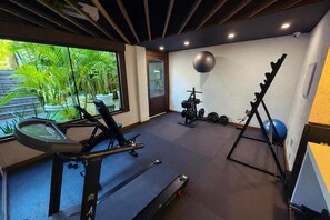A gym with exercise equipment, a treadmill, and a view of greenery outside. - Suri Búzios Hotel (Búzios)