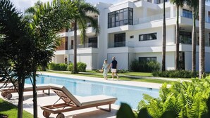 Un edificio moderno a più piani con area piscina, lettini e palme.