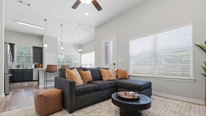 Un salon moderne avec un canapé d’angle, un pouf et une table basse.