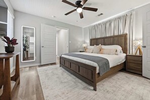 Ein Schlafzimmer mit Bett, Nachttischen, Deckenventilator, Spiegel und einer Tür.
