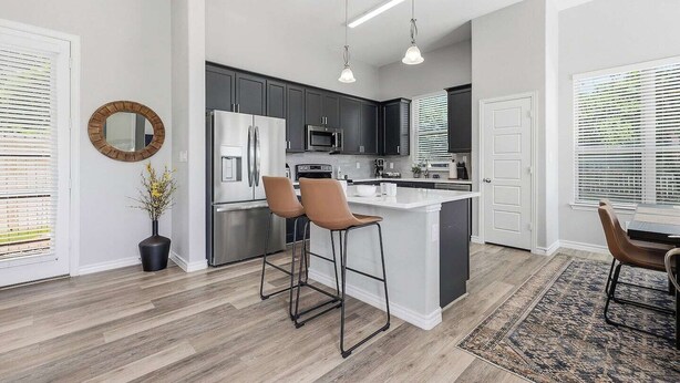 Une cuisine moderne dotée d’un îlot central, de meubles de couleur sombre, d’appareils électroménagers en acier inoxydable et de luminaires suspendus.