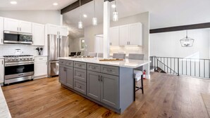 A modern kitchen with white cabinets, stainless steel appliances, and a large island. - Near Beach + Shopping • Tesla Charger • Large Deck (Kennebunkport)