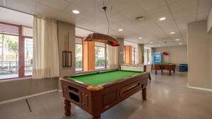 Un tavolo da biliardo in una stanza con finestre, un tavolo da calcio e un altro tavolo da biliardo.