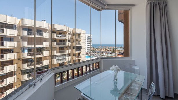 Un appartamento alto con balcone, ampie finestre e vista sul mare e altri edifici.