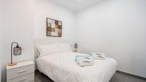 Una camera d'albergo ordinata con un letto, un comodino con una lampada, un quadro e un piccolo tavolino di sostegno.