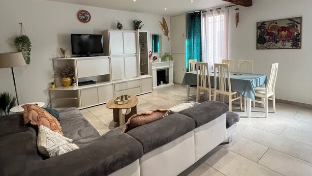 Een moderne woonkamer met een bank, televisie, kasten en een eethoek met stoelen en een tafel.