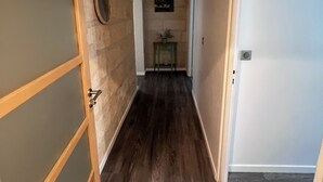 Een hal met houten vloer, een deur aan de rechterkant en een aan de muur bevestigd fotolijstje.