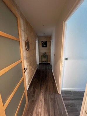 Ein Korridor mit Holzboden, einer Tür rechts und einem an der Wand befestigten Bilderrahmen.